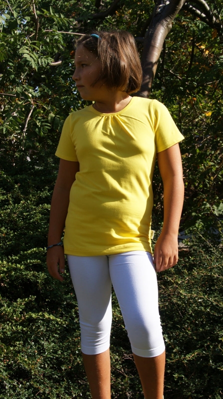 Dziewczynka w żółtej koszulce bawełnianej z krótkim rękawkiem, w stylizacji z białymi leginsami za kolanko, koszulka wykończona pod szyją lamówką, fason VKD-54.jpg
