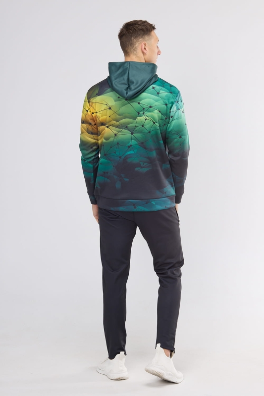 Model stojący tyłem w bluzie dresowej fason VBL-46, bluza nierozpinana z kapturem, kieszeń typu kangurka, grafika sportowa nr 4001, tło tonalna zieleń z czarną siatką, w stylizacji z długimi sportowymi czarnymi spodniami.jpg