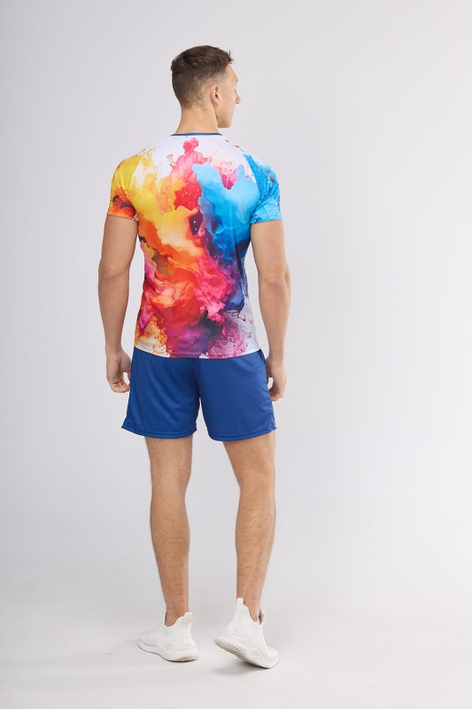 Model stojący tyłem w koszulce biegowej fason VKT-70-sub z grafiką Farba 4002, tło grafiki barwne eksplozje farby w odcieniach czerwieni, pomarańczu, żółci i niebieskiego, koszulka raglanowe wszycie rękawów, w stylizacji z granatowymi spodenkami.jpg