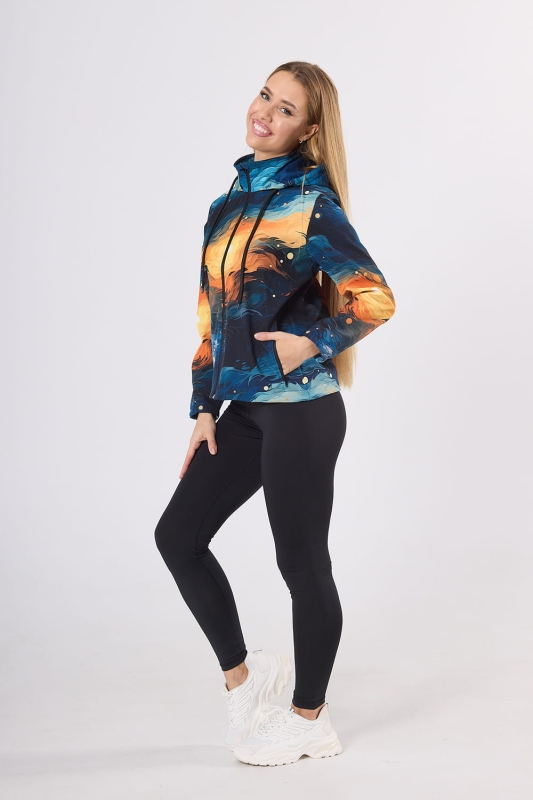 Modelka od boku w kurtce softshell fason VSOFTD-99 z grafiką 4004 w stylizacji z czarnymi leginsami, kurtka delikatnie taliowana, kaptur, zamek główny, dwie kieszenie z zamkami, nadruk pociągnięcia pędzla w barwach granatowy, pomarańczowy, żółty.jpg