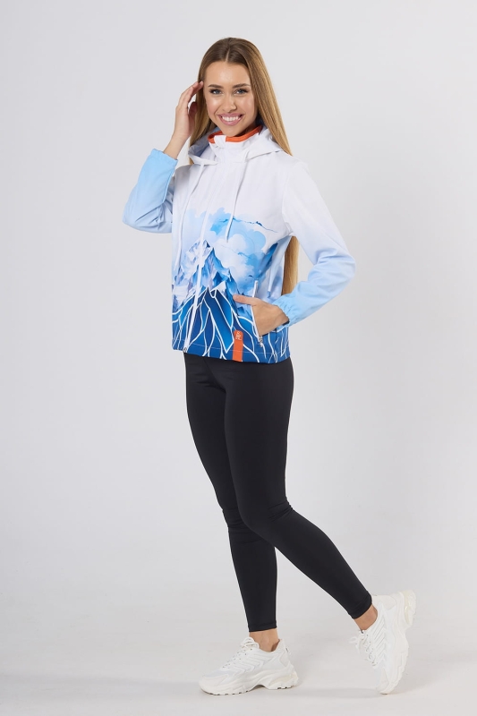 Modelka stojąca bokiem w kurtce softshell fason VSOFTD-99 z grafiką górskiego krajobrazu w barwach niebiesko-białych, kurtka zapinana  na zamek, dwie kieszenie z zamkami, doszyty kaptur z ozdobnym białym sznurkiem.jpg