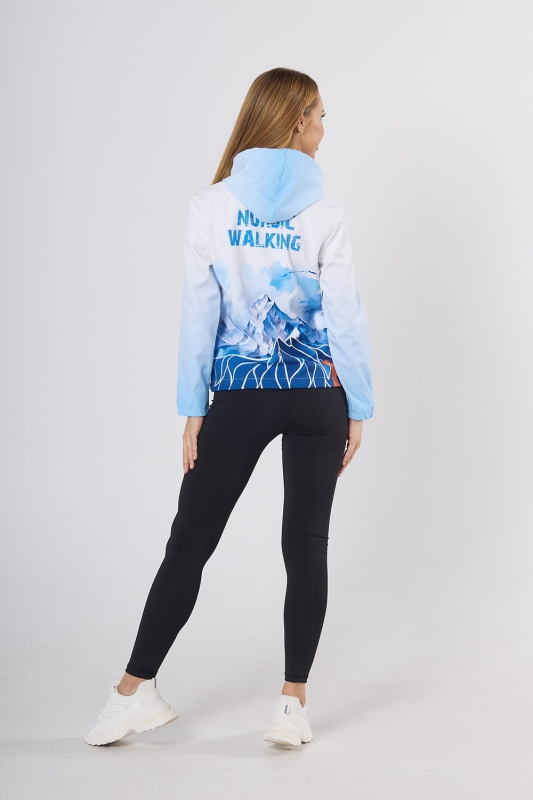 Modelka stojąca tyłem w kurtce softshell Nordic Walking  fason damski VSOFTD-99 z grafiką 4003 górskiego krajobrazu w barwach niebiesko-białych, kurtka w stylizacji z czarnymi leginsami.jpg