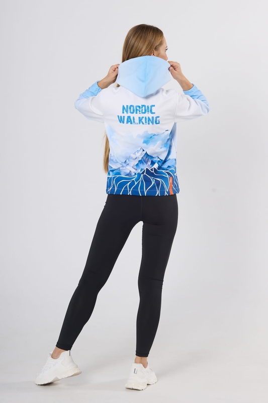 Modelka stojąca tyłem w kurtce softshell fason damski VSOFTD-99 z grafiką 4003 górskiego krajobrazu w barwach niebiesko-białych z niebieskim napisem Nordic Walking, kurtka w stylizacji z czarnymi leginsami.jpg