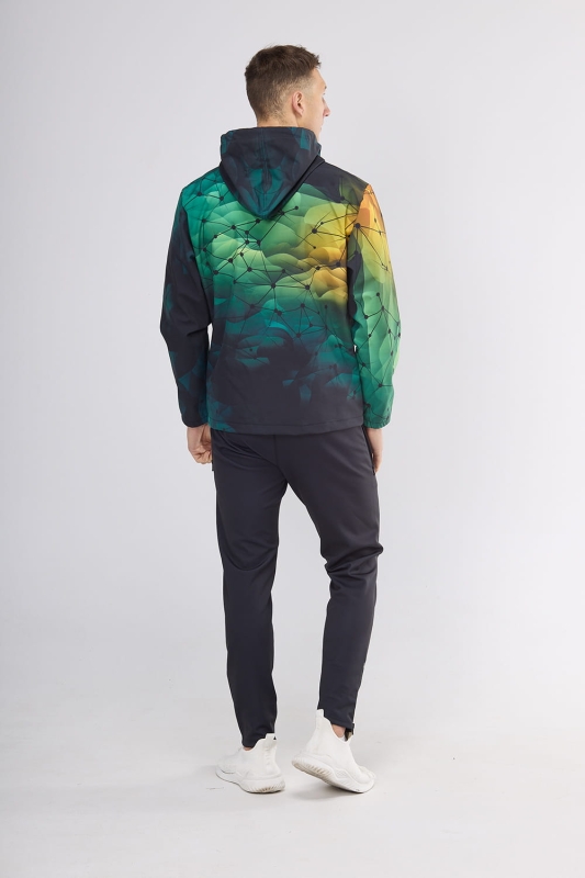 Model stojący tyłem w softshellu fason VSOFTM-99 z grafiką 4001, tło tonalne przejścia od ciemnej do jasnej zieleni z dodatkiem pomarańczowego, tło pokryte siatką geometryczną, kurtka z doszytym kapturem, w stylizacji z czarnymi spodniami sportowymi.jpg