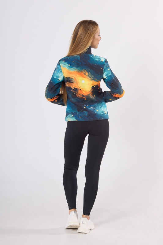 Modelka stojąca tyłem w kurtce softshell fason VSOFTD-98 z grafiką 4004 w stylizacji z czarnymi leginsami, grafika na kurtce maźnięcia pędzem w odcieniach niebieskich, pomarańczowych, żółtych, delikatnie taliowana.jpg