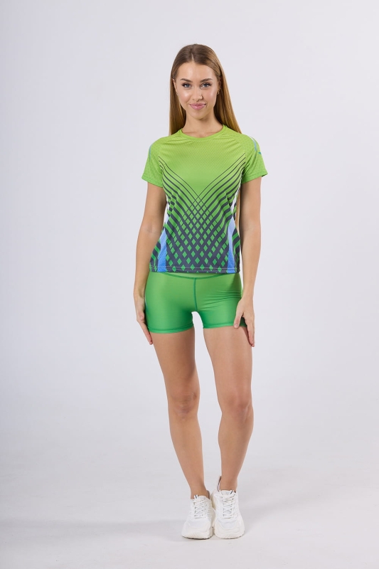 Modelka w koszulce sportowej z krótkim rękawem fason VKD-66 grafika 4010, raglanowe wszycie rękawów, kolor dominujący jasna soczysta zieleń, z  drobnym wzorem w postaci sześciokątów, w stylizacji z szortami w tych samych kolorach, tworzą komplet.jpg