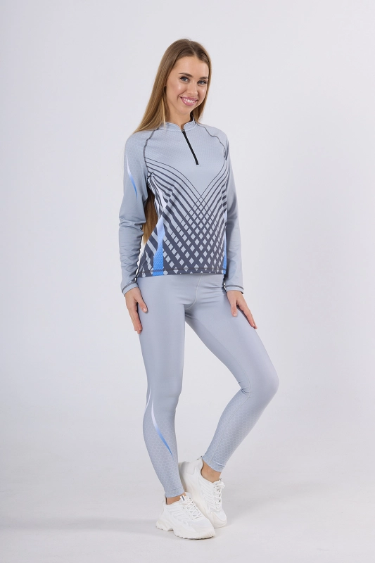 Sportowa stylizacja zaprezentowana na modelce. Longsleeve damski sportowy fason VKDRd-104 zapinanym na zamek 1/3, z delikatną stójką, w barwy jasno szare z geometrycznymi delikatnymi akcentami, w stylizacji z długimi szarymi leginsami,Ventus.jpg