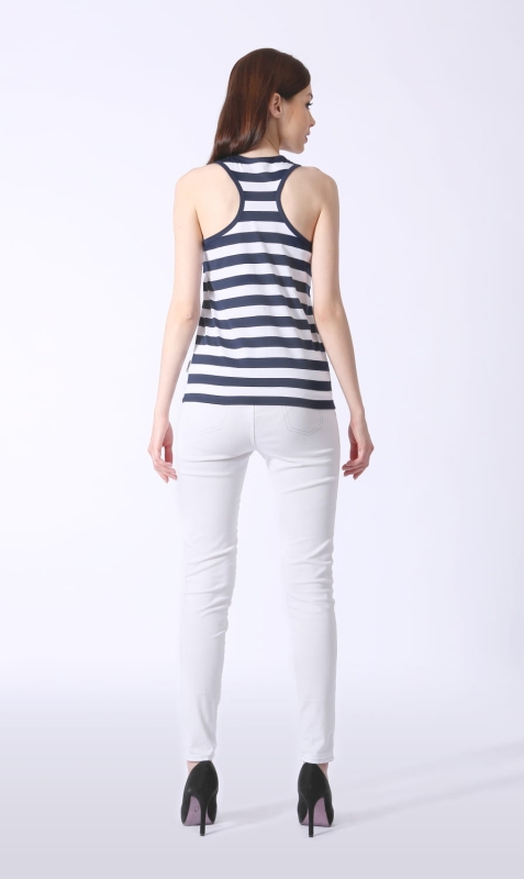 Modelka stojąca tyłem w tank topie damskim w paski biało-granatowe fason VKD-46, głębsze wycięcia na plecach, szerokość paska 2,5cm, koszulka delikatnie taliowana, modelka w stylizacji z białymi spodniami, styl żeglarski, marynarski.jpg