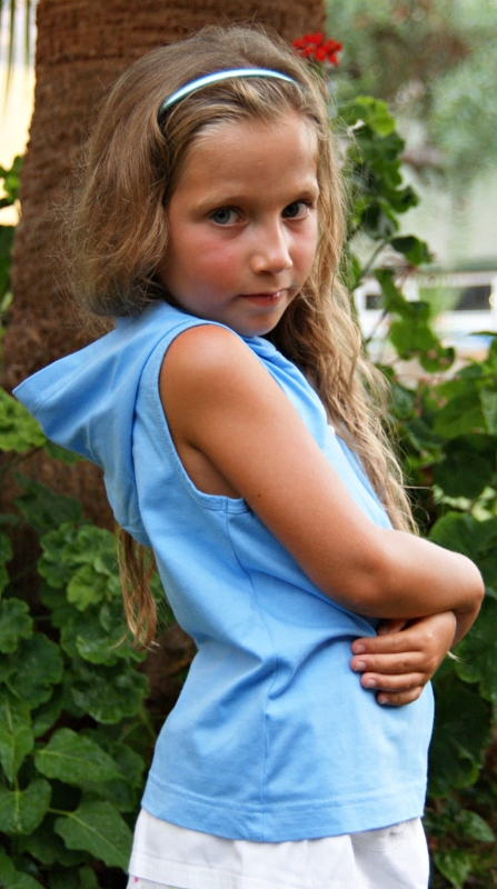 Dziewczynka stojąca bokiem w koszulce bez rękawków, z kapturem, zapinana na zamek 1/3 długości, bawełniana w kolorze niebieskim, fason VKD-4, pięknie komponuje się z bawełniana krótką spódniczką w białym kolorze.JPG