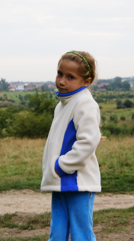 Polar dzieciecy fason unisex VPL-12 w kolorze białym z niebieskimi wstawkami po bokach, zapinany na zamek, stójka, bez kaptura, dwie kieszenie po bokach, polar zaprezentowany na dziewczynce.jpg