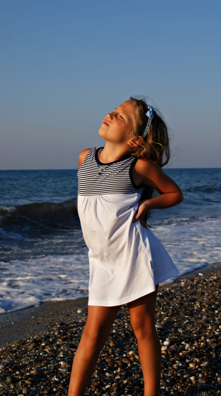 Dziewczynka w bawełnianej sukience letniej na ramiączkach, w stylu żeglarskim, góra w wąskie paski biało-granatowe, dół biały, sukienka do kolan, fason VS-2 marka Ventus.JPG